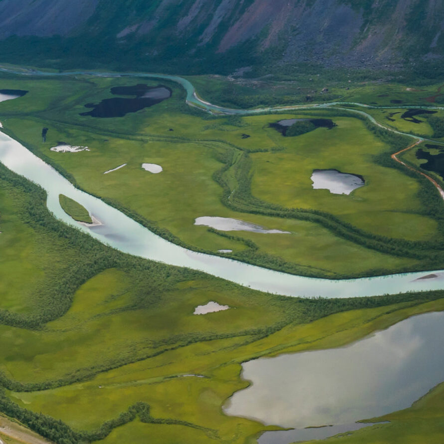 Aerial panoramic scenic view from Skierffe rock summit on glacial Rapadalen river delta valley at Sarek national park with meanders, lakes, mountains, birch trees. Summer day landscape Sweden Lapland